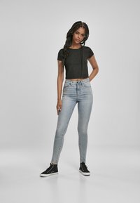Černé zkrácené tričko s texturovaným vzorem, v kombinaci se světle modrými skinny džíny a černými vysokými teniskami. Jednoduchý, neformální outfit.