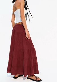 Burgundy, tierad maxikjol med en flödande design, tillverkad av lättviktsmaterial. Matchad med en vit kort topp och svarta sandaler.