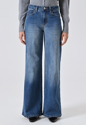 Jean en denim bleu à jambes larges et taille haute, avec une fermeture à bouton, cinq poches et des détails de décoloration subtils.