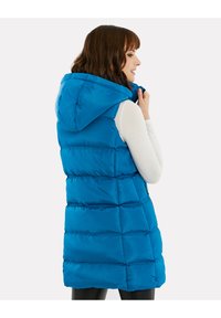 Blauer Puffer-Weste mit Kapuze, mit genähten horizontalen Abschnitten und einer glatten Textur. Das Model trägt darunter ein helles Oberteil.
