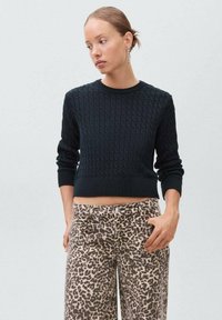 Maglione nero lavorato a maglia con scollo rotondo e lunghezza cropped, abbinato a jeans a vita alta con stampa leopardata e tasche frontali.