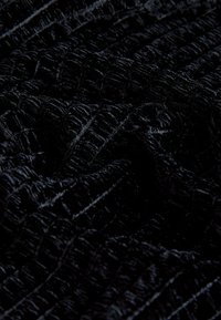 Sort tekstureret stof med et mønster af hævede, gitterlignende linjer og en blød og plyssede overflade.