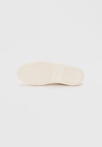 Suola di scarpa in gomma bianco sporco con motivi testurizzati, caratterizzata da un design piatto e bordi lisci; include branding sul lato.