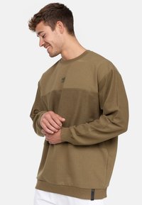 Khakifarbenes Sweatshirt mit strukturiertem Paneeldesign, langen Ärmeln, Rundhalsausschnitt und einem kleinen Logo-Patch auf der Brust.