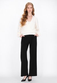 Witte wikkeltrui met lange mouwen, zwarte wijde broek en zwarte hoge hakken. Zachte textuur, minimalistisch ontwerp, neutrale kleuren.