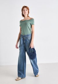 Grønn av-skuldret t-skjorte, høytlivte vide blå denimjeans og en marineblå vevd håndveske. Joggesko med en brun aksent.