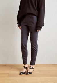 Námořnické slim-fit kalhoty v kombinaci s černými lodičkami se špičatou špičkou a kruhovými zlatými akcenty. Oblečení doplňuje černý oversized svetr.