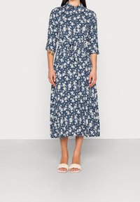 Blå blommig klänning med trekvartsärmar, knyt i midjan och en flödande kjol. Har ett vitt blommönster på blå bakgrund.