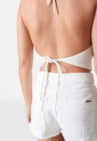 Witte gehaakte haltertop die aan de achterkant is vastgebonden, gecombineerd met hoge witte denim shorts met rafelige randen en twee achterzakken.