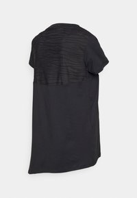 Camiseta negra de manga corta con panel trasero transparente y texturizado. La parte delantera es sólida con escote redondo y dobladillo curvado.