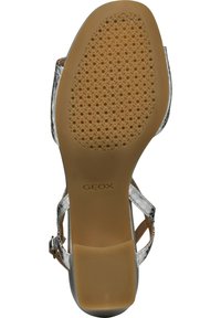 Sandalias Geox con una parte superior transparente, detalles de cuero marrón claro, una suela de goma texturizada y una correa de tobillo ajustable.