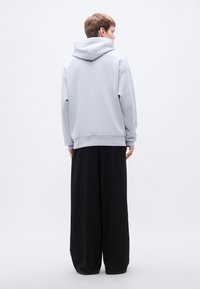 Ανοιχτό γκρι φούτερ με μεγάλη κουκούλα, χαλαρή εφαρμογή και ριμπ μανσέτες, συνδυασμένο με φαρδιά μαύρα παντελόνια σε ένα ρέον, άνετο σιλουέτα.