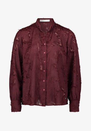 Długi rękaw ciemnoczerwonej bluzki z fakturowanej tkaniny z frędzlami, z przodem zapinanym na guziki i małym stojącym kołnierzykiem.