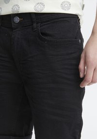 Jean en denim noir avec une coupe slim, des passants de ceinture, des poches avant et une légère texture. Pas de marque ou de décorations visibles.