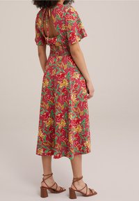Czerwona sukienka w kwiaty z krótkimi rękawami, marszczoną talią i otwartym tyłem. Posiada żółte i zielone wzory kwiatowe. Połączona z brązowymi sandałami na słupku.
