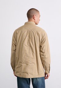 Long-sleeve shirt in beige with vertical blue and white stripes. Features a relaxed fit, button-down collar, and single back pleat.