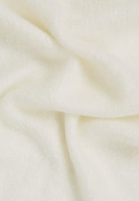 Tecido moale de culoare crem, cu o textură ușor pufoasă și pliuri delicate care creează umbre și accente subtile.