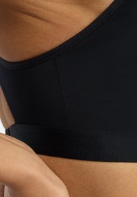 Soutien-gorge de sport noir avec un tissu lisse et extensible. Il possède une large bande plate en bas et un détail de couture minimal le long des bords.