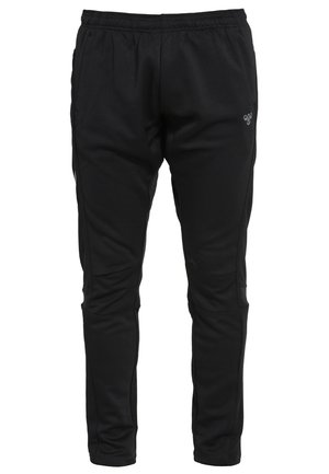 Atletische man joggend in een zwart mouwloos shirt, zwarte sportbroek met zij-chevron ontwerp, en zwarte hardloopschoenen tegen een effen achtergrond.