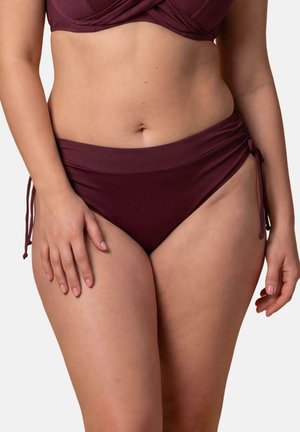 Kobieta nosząca bordo dół bikini z wiązaniami po bokach i pasujący górny części bikini, pokazana od połowy tułowia do górnej części ud.