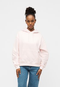 Φωτεινό ροζ φούτερ με μπροστινή τσέπη, κουκούλα με κορδόνι και ριμπ μανσέτες, σε συνδυασμό με μπλε τζιν παντελόνι φαρδιάς γραμμής. Μαλακό, casual ύφασμα.