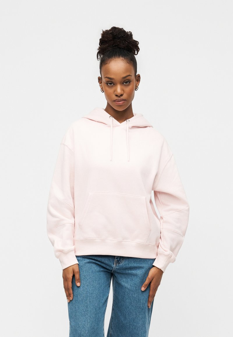 Φωτεινό ροζ φούτερ με μπροστινή τσέπη, κουκούλα με κορδόνι και ριμπ μανσέτες, σε συνδυασμό με μπλε τζιν παντελόνι φαρδιάς γραμμής. Μαλακό, casual ύφασμα.