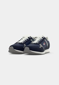 Marineblauwe sneakers met een mix van suède en mesh materialen, voorzien van witte veters, een grijze zool en een logo patch aan de zijkant.