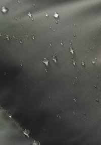 Wasserabweisender Stoff in Dunkelgrau mit strukturierter Oberfläche, auf der verstreute Wassertropfen die feuchtigkeitsabweisende Eigenschaft hervorheben.