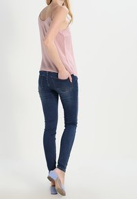 Růžový top bez rukávů s volnějším střihem, zkombinovaný s tmavě modrými úzkými džíny s květinovým vzorem a světlými botami na širokém podpatku.