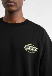 Czarny bawełniany t-shirt z logo w kolorze żółtym i białym, okrągłym dekoltem i krótkimi rękawami. Materiał ma gładką teksturę.