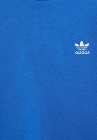 Modrá bavlněná tričko s kulatým výstřihem a malým bílým logem Adidas na levé hrudi. Textura vypadá hladce a lehce.