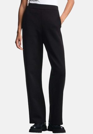 Schwarze weit geschnittene Hosen aus weichem Material, mit hohem Bund und seitlichen Taschen, kombiniert mit schwarzen klobigen Schuhen.