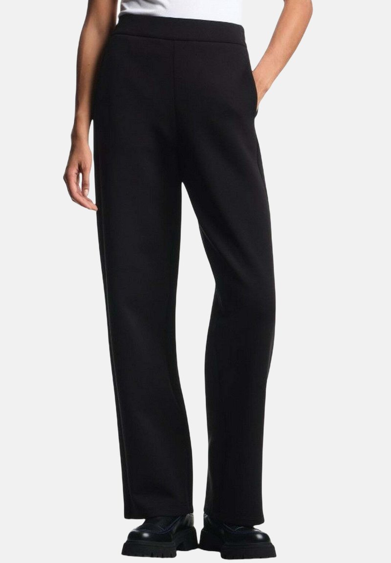 Pantaloni neri a gamba larga in tessuto morbido, con vita alta e tasche laterali, abbinati a scarpe nere chunky.