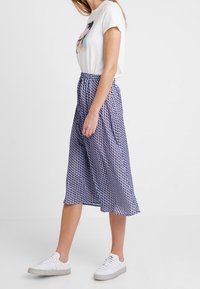 T-shirt bianco con un design colorato, abbinato a una gonna midi di lunghezza al polpaccio con un motivo geometrico in viola e bianco. Sneakers bianche.