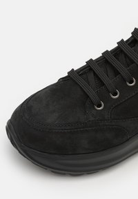 Svart semsket sneakers med avrundet tå, teksturert overdel, metalløyer og svarte lisser, med en tykk gummisåle for demping.
