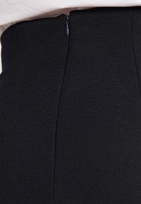 Jupe noire à taille haute en tissu texturé, avec une fermeture à glissière dissimulée au dos et des lignes lisses et épurées.