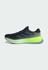 Chaussure de sport noire et grise avec semelle vert néon et bleue, dessus en mesh et trois bandes foncées sur le côté.
