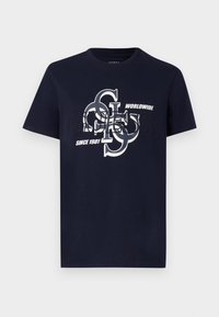 Camiseta de algodón azul marino con mangas cortas que presenta un diseño de logotipo gráfico en blanco. El texto incluye "Guess", "Worldwide" y "Since 1981."