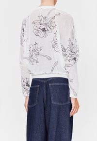 Lättvit långärmad topp med svart blommönster, med avslappnad passform och ribbade ärmslut, ihop med mörkblå vida jeans.