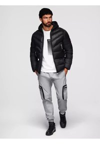 Giacca a vento nera con cappuccio, dotata di tasche con zip. Abbinate a pantaloni cargo grigi chiari con dettagli neri e sneakers alte nere.