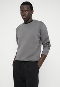 Sivá mikina s okrúhlym výstrihom, rebrovanými manžetami a voľným strihom, spárovaná s čiernymi nohavicami so sťahovacou šnúrkou. Mäkko štruktúrovaná tkanina.