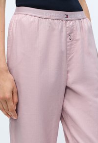 Rosa pyjamasbyxor med en lätt textur, featuring ett elastiskt midjeband med "TOMMY HILFIGER"-logotyp och en knappdetalj fram.