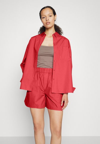 Rød skjorte med oppbrettede ermer, knappet front og brystlomme, kombinert med røde shorts. Begge er laget av lett stoff.