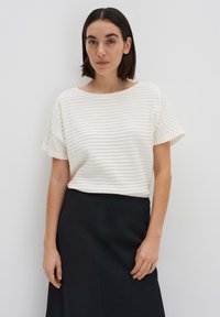 Witte textuur short-sleeve top met een brede halslijn, gecombineerd met een zwarte rok, wat een contrast in kleur en textuur creëert.
