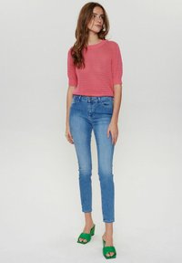 Rozā adīta īsām piedurknēm džemperis kombinēts ar gaiši ziliem šauriem džinsiem un zaļiem augstiem zābakiem, ar apaļu kakla izgriezumu un viļņveida maliņām.