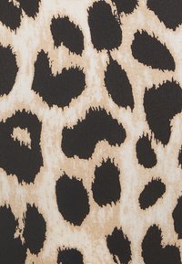 Le tissu à imprimé léopard présente des taches noires irrégulières sur un fond beige. La texture semble lisse avec un léger éclat.