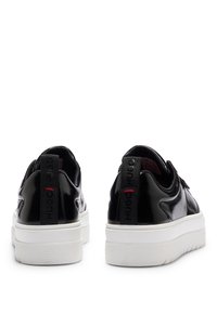 Schwaze Lackledersneaker mit weißen Gummisohlen, ausgestattet mit einem Logo-Tag auf der Rückseite, glatter Oberfläche und minimalistischem Design.