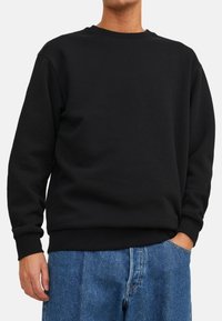 Sweatshirt noir en mélange de coton, avec col rond, manches longues, poignets et ourlet à côtes, associé à un jean en denim bleu clair.