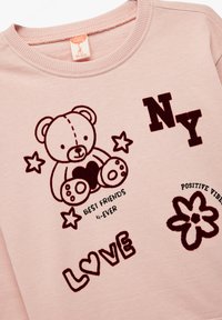Roze sweatshirt met een teddybeerafbeelding met een hart, en tekst elementen zoals "BEST FRIENDS 4-EVER," "NY," en "LOVE" in donkerbruin.