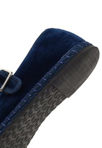 Granatowe zamszowe mokasyny z srebrną klamrą, z wyraźnym niebieskim przeszyciem wzdłuż podeszwy i teksturowaną czarną gumową podeszwą.
